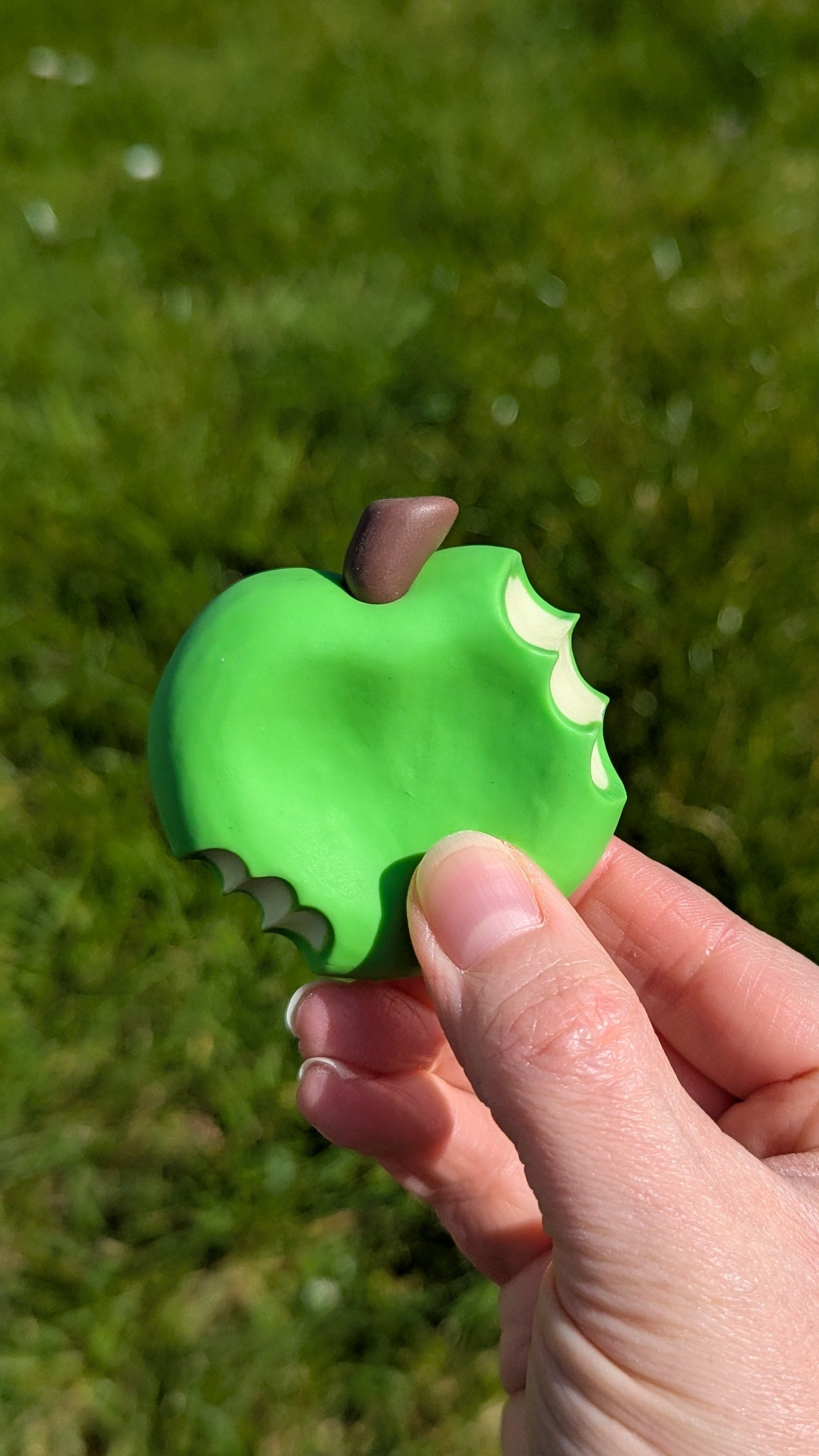 Hand holding a green apple-shaped object against a grassy background